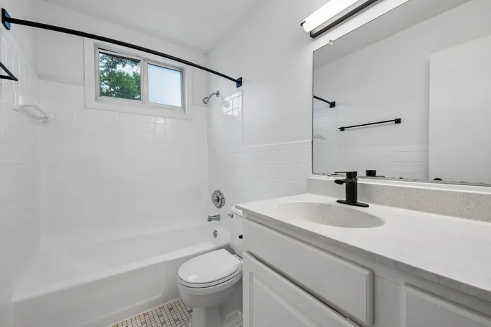 Bright and modern bathroom featuring sleek white tiles, an elegant vanity, and natural light from a stylish window.