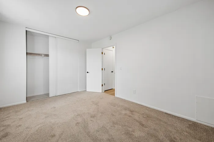 Bright and welcoming bedroom with plush carpeting, spacious closet, and modern lighting fixture.
