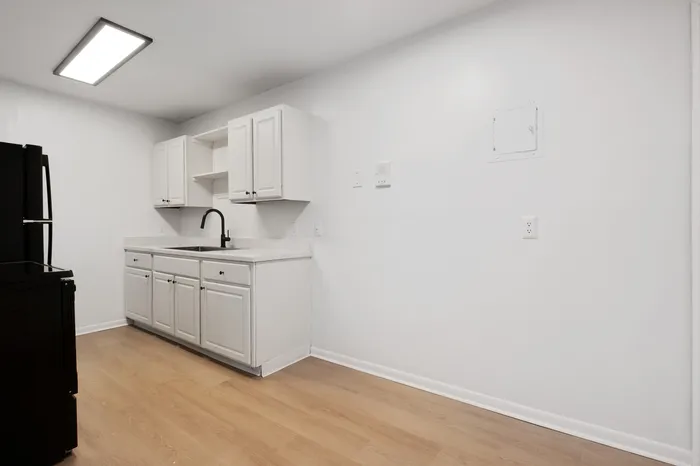 Modern kitchen with sleek white cabinetry, elegant black fixtures, and warm wood flooring, creating a bright and inviting space.