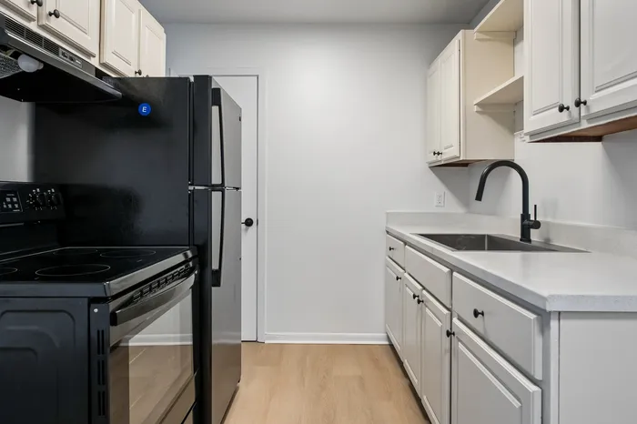 Sleek modern kitchen with black appliances, elegant white cabinetry, and stylish wood flooring.