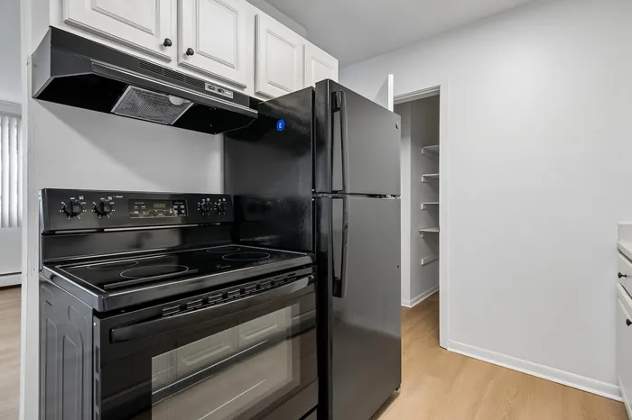 Modern kitchen with sleek black appliances, bright white cabinets, and a spacious pantry area.