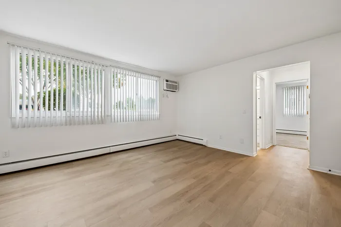 Bright and inviting living space with large windows, sleek hardwood floors, and modern air conditioning unit.