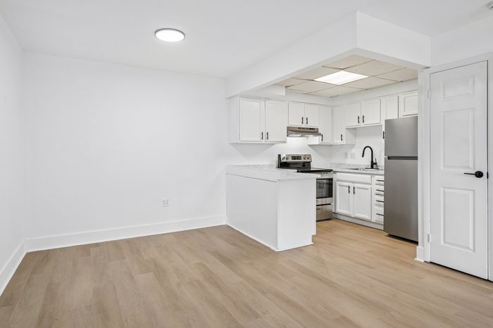 Modern apartment kitchen with sleek white cabinets, stainless steel appliances, and stylish wooden flooring.