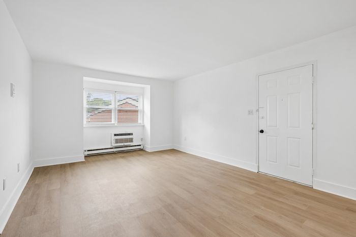 Bright and airy room with elegant hardwood floors and large window, offering abundant natural light in a modern setting.