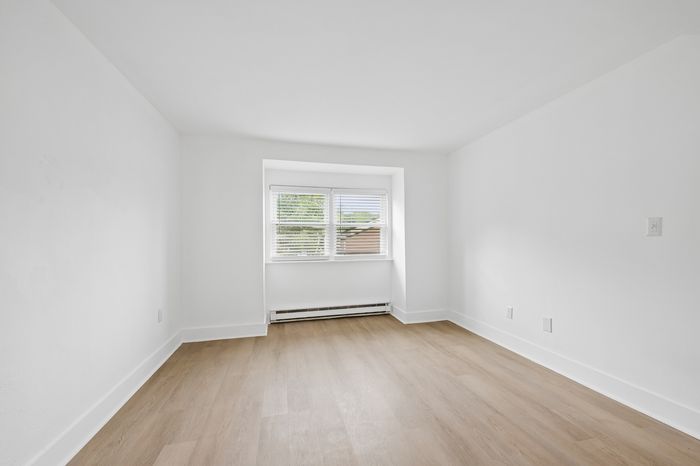 Bright and airy room with elegant hardwood floors and a large window, perfect for creating a cozy living space.