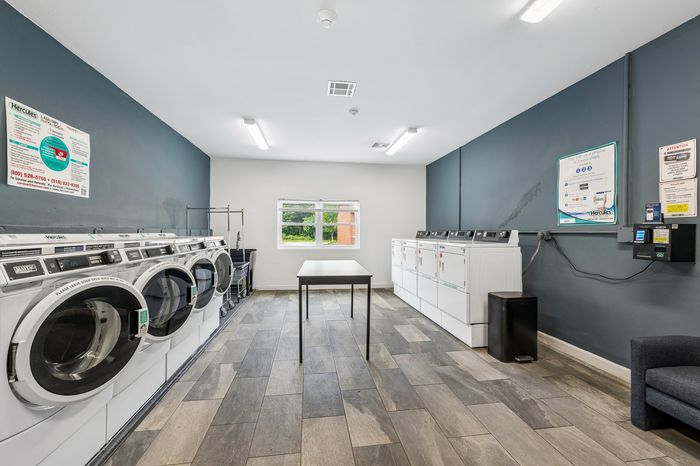 Modern, spacious laundry room equipped with multiple washers and dryers, sleek flooring, and ample folding space for convenience.