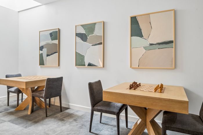 Elegant interior showcasing modern art above stylish wooden tables with chess setups, complemented by sleek chairs and soft, neutral-toned decor.