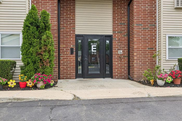 Charming apartment entrance with brick facade and vibrant potted flowers, exuding a welcoming atmosphere.