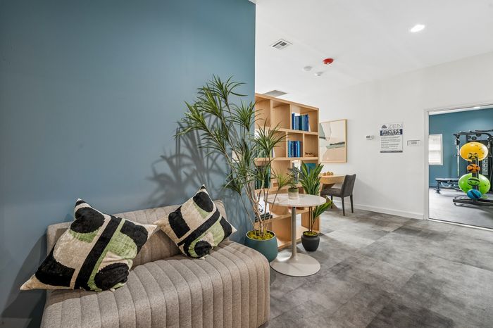 Inviting apartment nook with modern seating, stylish decor, and open view of a well-equipped gym.
