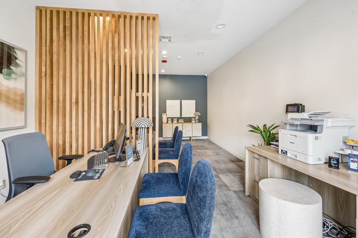 Modern office space with sleek wooden accents, stylish blue chairs, and a well-organized desk area perfect for productive work sessions.