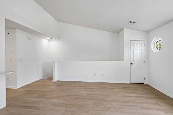 Bright and spacious living area with elegant wood flooring, modern white walls, and a stylish octagonal window.