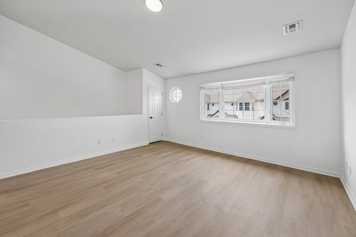 Bright and spacious room with elegant wood flooring, large window, and modern white walls, perfect for a cozy living space.