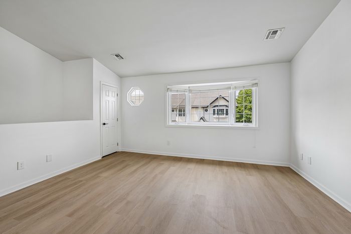 Bright and airy room with elegant hardwood floors, large windows with a scenic view, and modern white walls.
