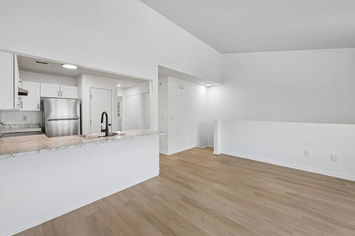 Bright modern apartment interior featuring an open kitchen with sleek stainless steel appliances and a spacious living area with elegant wooden flooring.