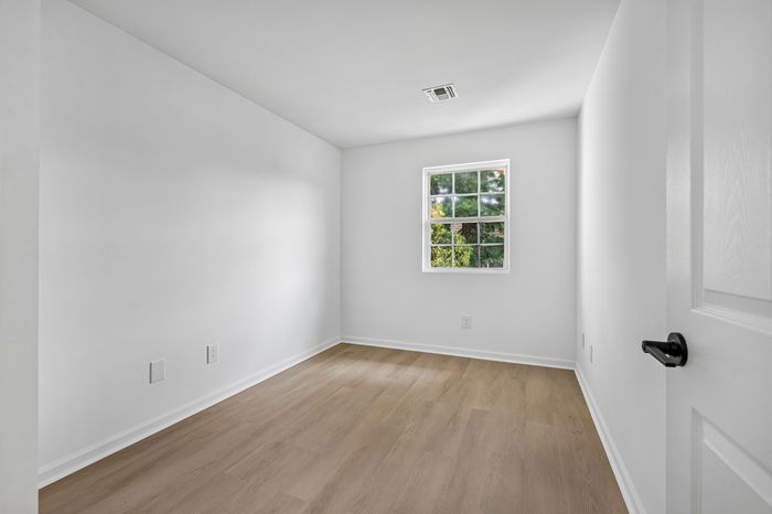 Bright and airy room with pristine white walls, a large window providing natural light, and elegant hardwood floors, perfect for a cozy and serene living space.