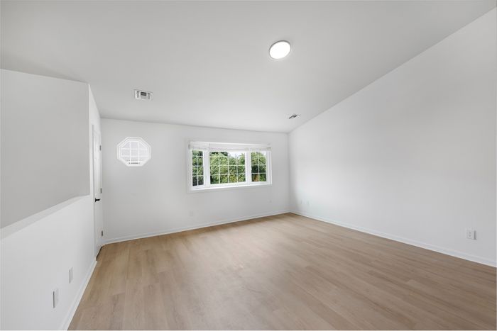 Bright and spacious room with sleek wooden flooring and large windows, offering abundant natural light and garden views.