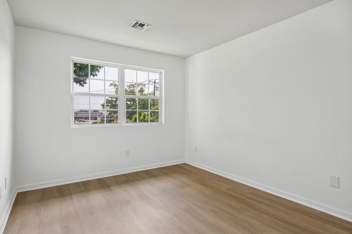 Bright, empty room featuring modern wood flooring and a large window offering a serene outdoor view.