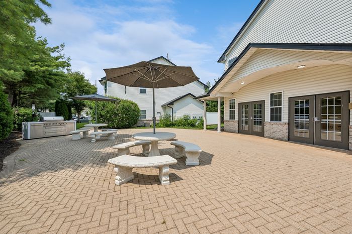 Inviting outdoor communal space featuring stylish stone benches, large umbrellas, and a modern barbecue area, perfect for gatherings and relaxation.