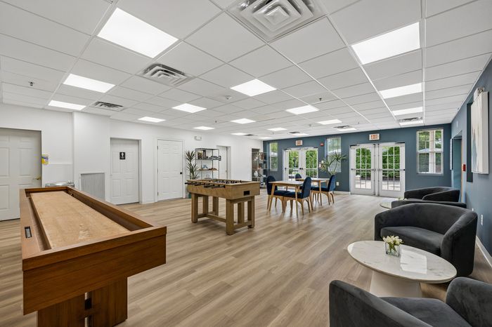 Bright and inviting community room featuring stylish game tables, modern seating, and large windows for natural light.