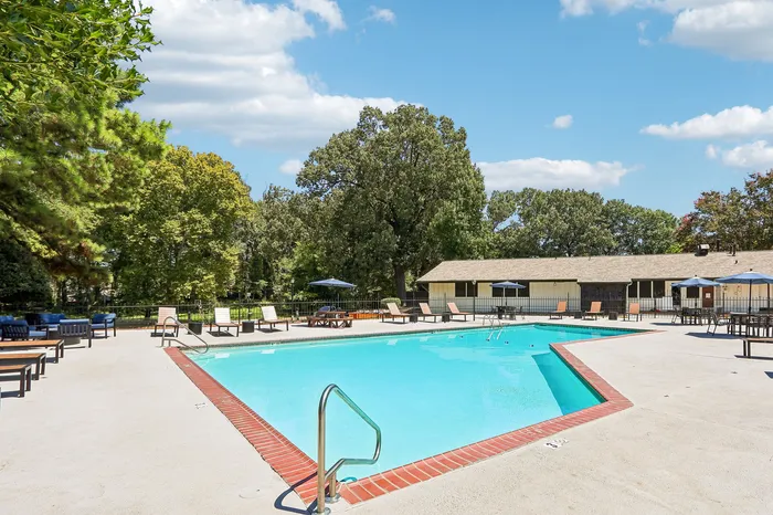 Inviting outdoor retreat with a sparkling pool, surrounded by lush greenery and lounge chairs under blue umbrellas.