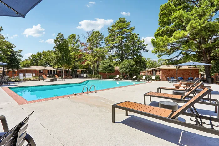 Inviting outdoor pool area with modern lounge chairs, surrounded by lush trees and a clear blue sky.