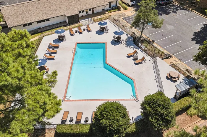 Inviting aerial view of a sunlit swimming pool surrounded by stylish lounge chairs and lush greenery, perfect for relaxation in a serene apartment complex setting.
