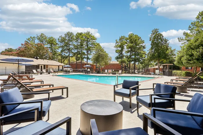 Luxurious outdoor pool area with stylish seating, surrounded by lush greenery and clear blue skies, ideal for relaxation and leisure.