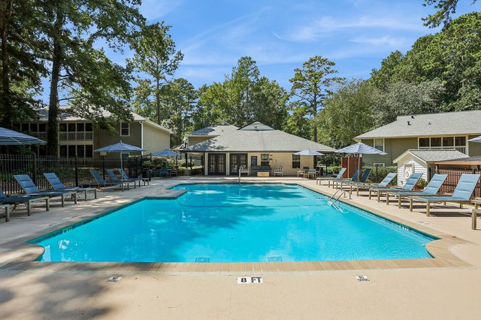 Inviting outdoor pool area surrounded by lush greenery, featuring numerous loungers and umbrellas for relaxation.