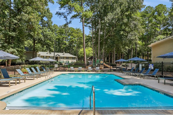 Inviting outdoor pool area surrounded by lush greenery and comfortable lounge chairs, set within a serene and picturesque residential community.