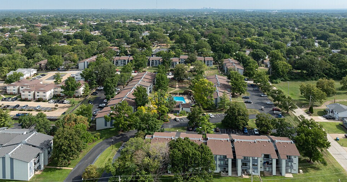 Aerial view of a vibrant apartment community surrounded by lush greenery, featuring a central swimming pool and ample parking space.