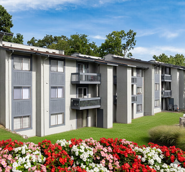 Charming apartment building with private balconies, surrounded by vibrant flower beds and lush greenery, offering a serene living experience.