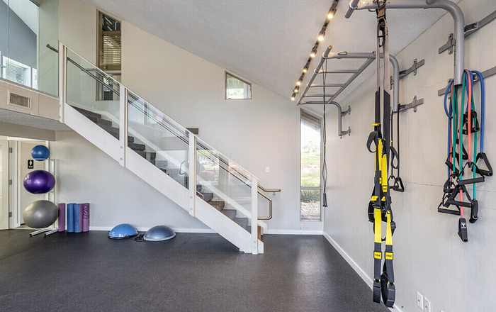 Bright and modern home gym with sleek equipment, TRX suspension trainers, and exercise balls, under stylish staircase.