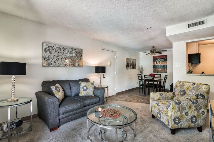 Inviting living room with modern decor, showcasing a cozy gray sofa, patterned armchair, and chic glass coffee table, perfect for relaxation and entertaining.