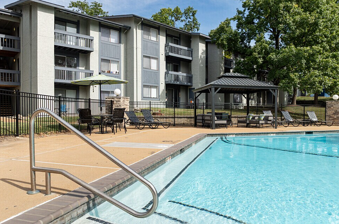 Inviting apartment complex with a refreshing swimming pool, shaded seating area, and modern lounge chairs, perfect for relaxation and socializing.