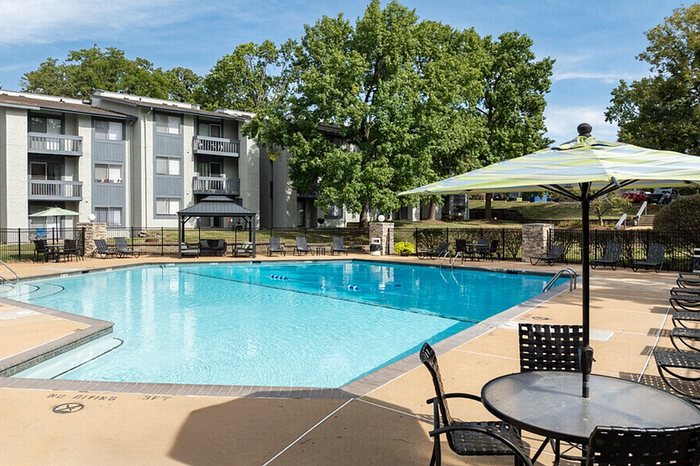 Inviting outdoor pool area with ample seating, surrounded by lush greenery and modern apartment buildings.