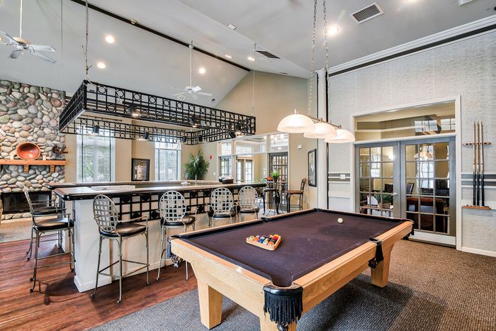 Chic entertainment space featuring a pool table, elegant bar seating, and cozy stone fireplace.