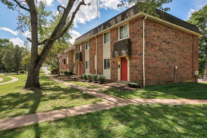 Charming brick apartment building with red doors, nestled in a lush green setting, offering a cozy and inviting living environment.