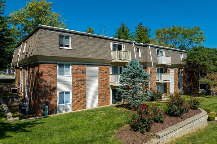 Charming brick apartment building with lush greenery and vibrant flowers, offering a welcoming ambiance and scenic views.