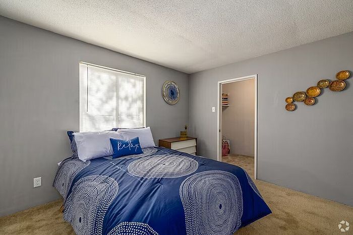 Bright and inviting bedroom featuring chic decor, a cozy bed with a modern blue comforter, and natural light filtering through a large window.