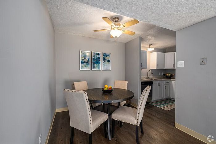 Chic dining area with elegant round table and plush chairs adjacent to a contemporary kitchen, bathed in ambient light from a stylish ceiling fan.