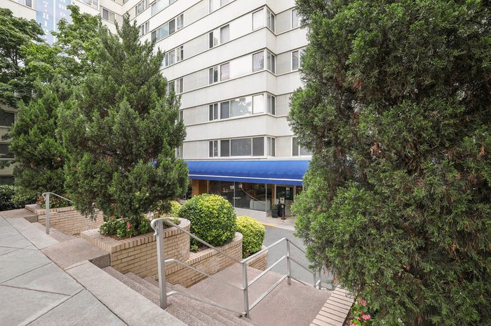 Inviting apartment entrance with lush greenery, elegant stairs, and modern exterior design.