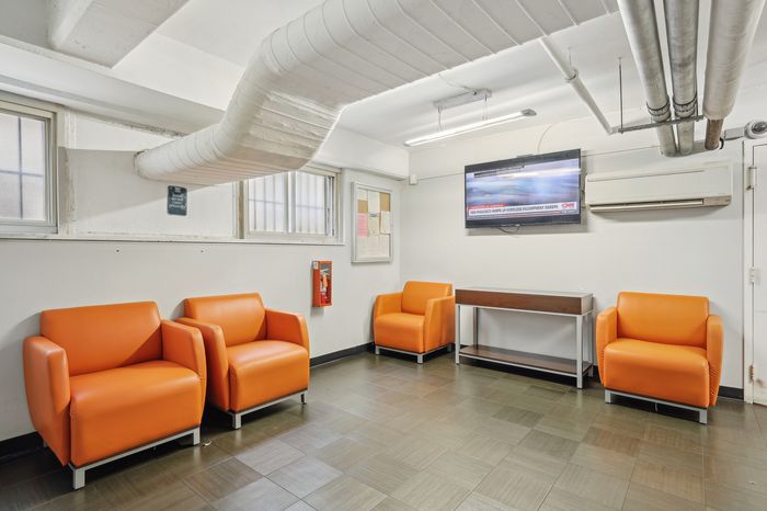 Modern lounge area featuring vibrant orange armchairs, sleek tiled flooring, wall-mounted TV, and contemporary design elements.
