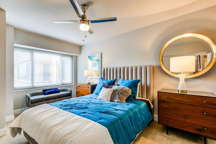 Elegant bedroom with plush blue bedding, stylish wooden furniture, and a large window inviting natural light, showcasing modern comfort and sophistication.