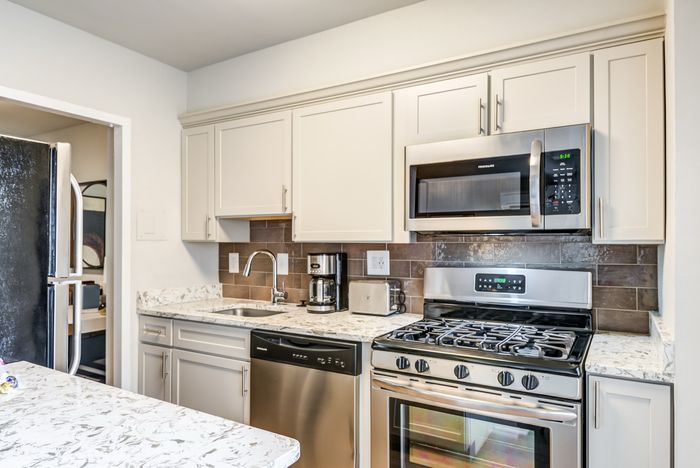 Contemporary kitchen with sleek stainless steel appliances, elegant white cabinetry, and a marbled countertop for a sophisticated look.