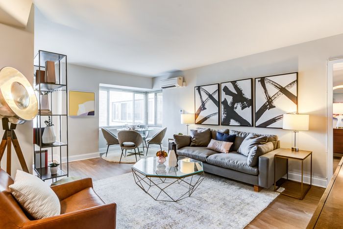 Elegant living room with modern accents, featuring a comfortable gray sofa, abstract artwork, and a cozy dining nook with corner windows.