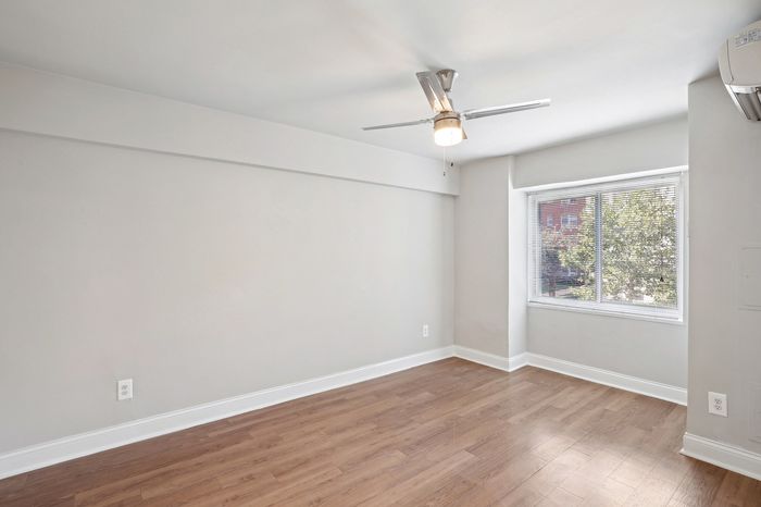Bright and airy room with elegant wooden flooring, large window, and modern ceiling fan, perfect for comfortable living.
