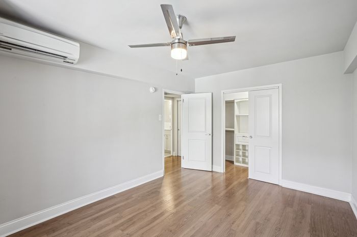 Bright bedroom with elegant wooden flooring, featuring a modern ceiling fan and a spacious closet, perfect for comfortable living.