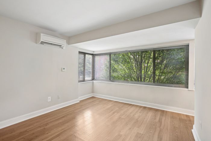 Bright and airy room with large windows, elegant hardwood floors, and modern air conditioning unit.