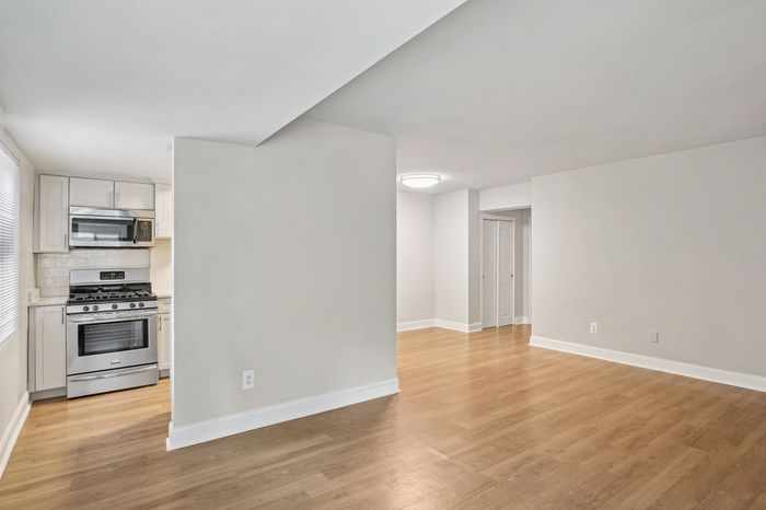 Modern apartment kitchen with sleek appliances adjacent to a bright, open living area featuring stylish wood flooring.