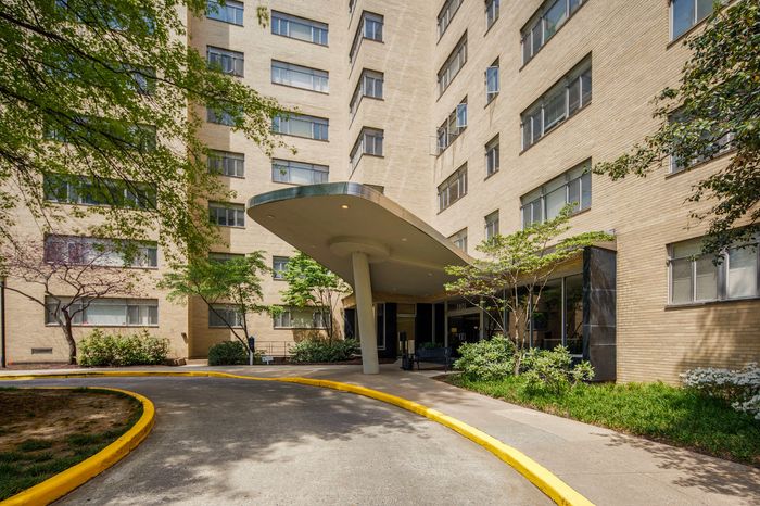 Charming apartment building entrance with a sleek covered walkway surrounded by lush greenery.